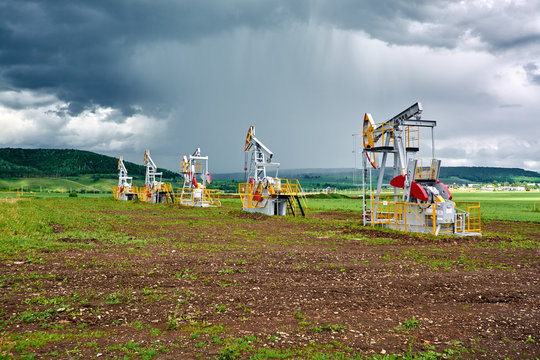 Pumping unit for pumping oil on a background of cumulus clouds and rainfall