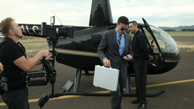 Behind the scenes, camera operator shoots a businessman getting out of a helicopter