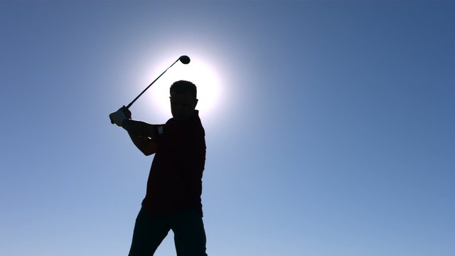 Silhouette of golfer teeing off, slow motion