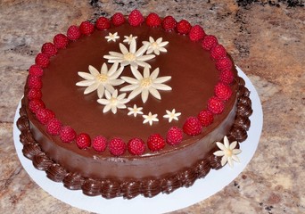 Dark chocolate cake decorated with white fondant flowers and fresh raspberries