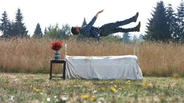 Man falling onto bed in field, slow motion