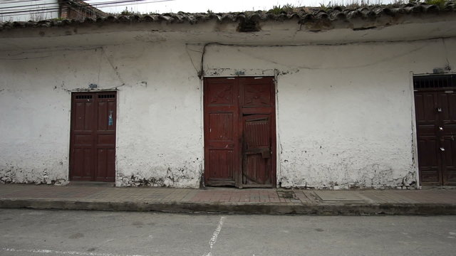 Panning shot of an old dilapidated adobe style colonial era building situated on a modern day asphalt street.