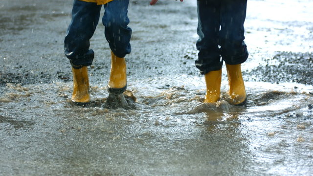 Two young boys jumping in mud puddle