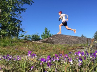 trail runner on rocky outcrop with purple flowers in foreground