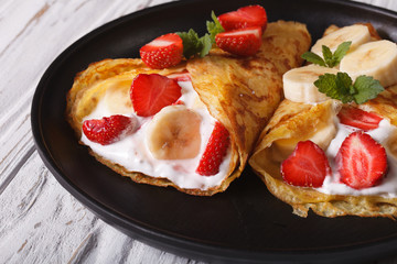 crepes with strawberries, bananas and cream close-up on a plate