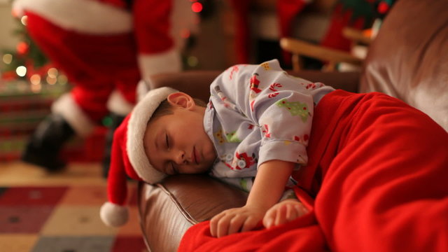 Boys sleeps on Christmas eve with Santa Claus in background