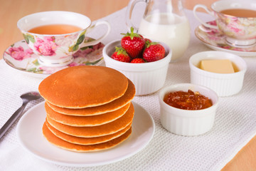 Stack of pancakes with fresh strawberries; butter, marmelade, an