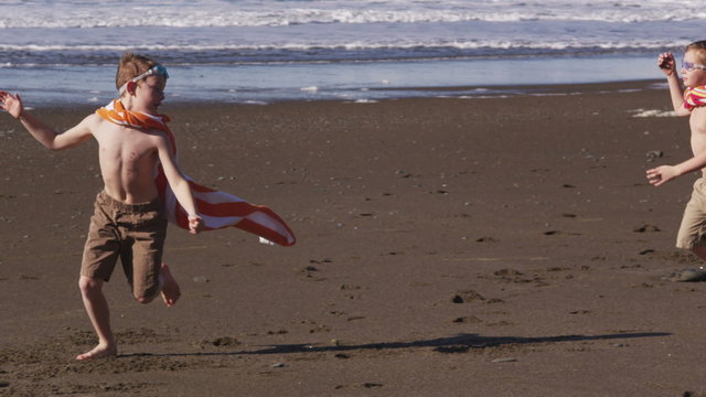 Young boys running at beach with superhero costumes