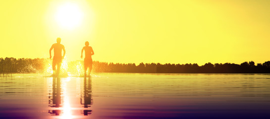 Glückliche junge Menschen laufen und springen am See beim Sonnenuntergang