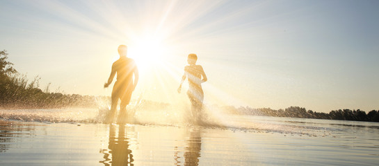 Glückliche junge Menschen laufen und springen am See beim Sonnenuntergang