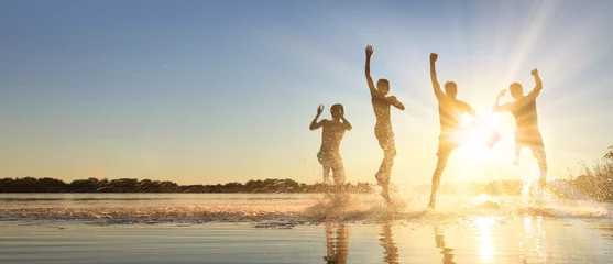 Fototapeten Glückliche junge Menschen laufen und springen am See beim Sonnenuntergang © Thaut Images
