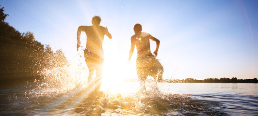 Glückliche junge Menschen laufen und springen am See beim Sonnenuntergang © Thaut Images