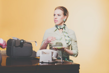 Retro 50s young blonde secretary woman sitting behind desk drink