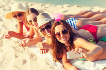 group of smiling women with smartphone on beach