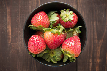 Top view fresh strawberries in a bowl on wooden background.
