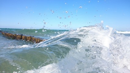Welle wird von Bunen gebrochen - Wellenbrecher an der Küste