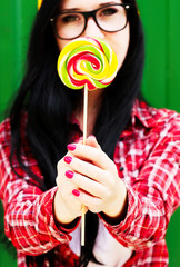 Fashion girl hipster in glasses and shirt with candy outdoors