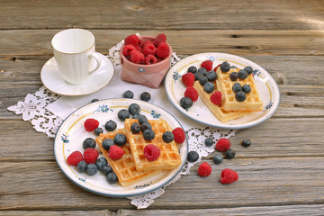 Waffles with raspberries and blueberries for breakfast on wood background