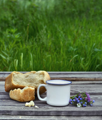 Cup of milk with bread and bunch of flowers on planks 