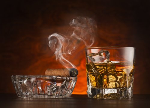 Glass of whiskey ice and cigar on wooden surface