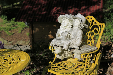 Barocke Gartengestaltung: Skulptur eines verträumten jungen Paares im gelben Stuhl sitzend