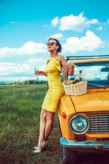 Beautiful woman on the picnic is drinking wine near a car.
