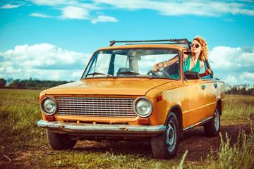 Woman is driving an old yellow car. Rural background.