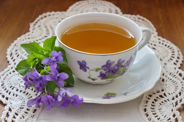 china tea cup with pattern of violets and bouquet of violets on the white tablecloth