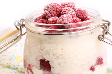 breakfast rice porridge with vanilla sauce, frozen raspberries in a glass jar white background
