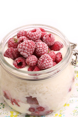 breakfast rice porridge with vanilla sauce, frozen raspberries in a glass jar white background