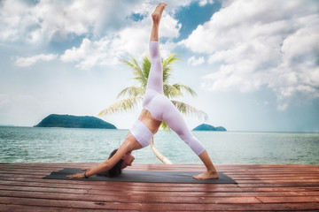Young woman doing yoga asana at pier of tourist resort