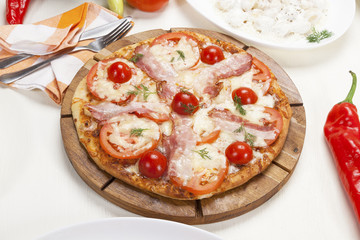 Pizza with bacon, feta and tomato served on a table.