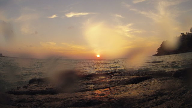 Timelapse del tramonto visto da sopra uno scoglio con schizzi d'acqua e i granghi che passeggiano