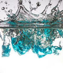 blue ice cubes dropped into water with splash 