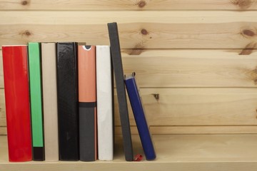 Shelf with different colored books on a wooden background

