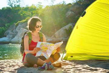 Happy young woman tourist nearby the tent looking into map