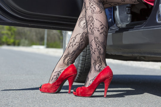 Feet Of Stylish Female Driver Walking Out Of Car. Female Leg Dressed Provocative Clubbing Pantyhose High Heels Red Shoes Step Out Of The Blue Car