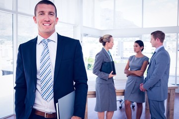 Fototapeta premium Businessman smiling at camera with colleagues behind him