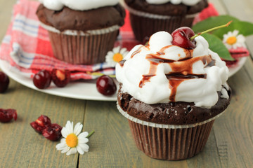 Chocolate cupcakes with cherries on wooden background. top view