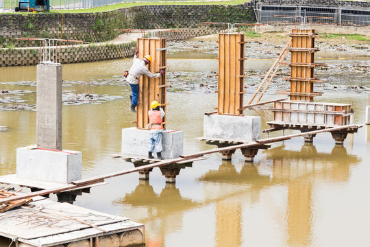 Workers building bridge foundation across lake