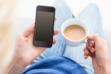 Woman using her mobile phone and holding cup of coffee