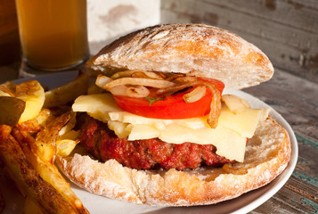 Home made barbecued beef burger topped with fried onion, tomato and cheese served with fries and beer. A tasty meal perfect for a summer day in the garden by the barbeque.
