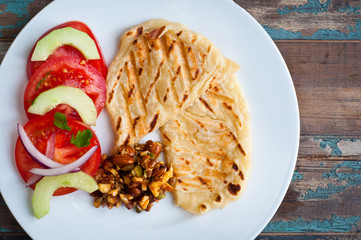 Healthy snack, side dish of roasted, spiced chick peas, home made flat bread and sliced tomato and cucumber salad.