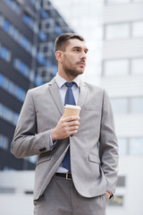 young serious businessman with paper cup outdoors