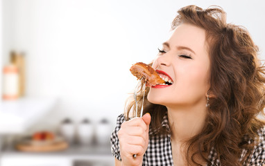 hungry young woman eating meat on fork in kitchen