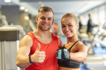 Foto op Plexiglas smiling man and woman showing thumbs up in gym © Syda Productions
