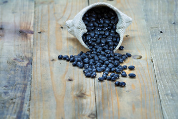 Fototapeta na wymiar Black beans in sack on vintage wooden boards