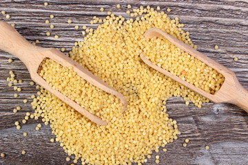 Heap of millet groats with spoon on wooden background