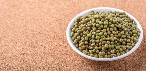 Mung beans in white bowl on cork board background