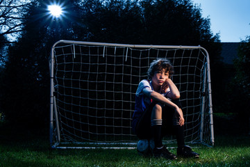 soccer player sitting in front of the net on his soccer ball